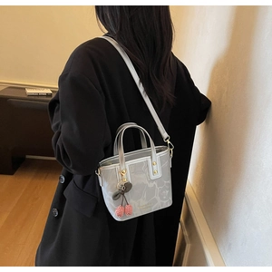 Detail of grey marble pattern tote bag with cherry charm worn over a black winter coat