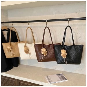 Detail of woven tote bags in four colors with cute teddy bear charms hanging on a rack