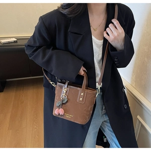 Brown leather bucket bag with cherry charm shown on model in black blazer and jeans