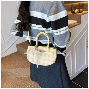 Close-up of yellow checkered bucket bag with lace bow and pearl charm on a model