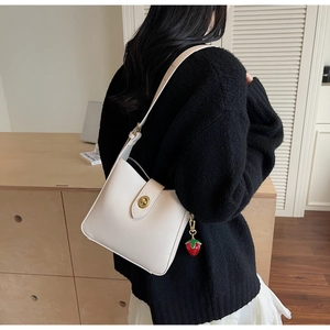 Detalle de bolso hobo de cuero crema con cierre de anillo dorado y colgante de fresa
