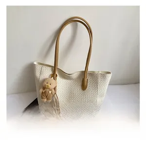 Close-up of white woven tote bag with brown straps and cute bear charm decoration