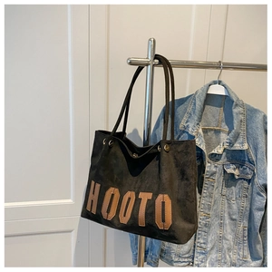 Detail of black suede tote bag with HOOTO letter patch hanging beside a denim jacket