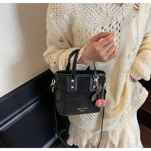 Detail of black mini bucket bag with floral patterns and cherry charm on PU leather
