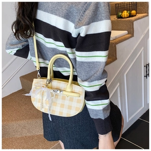 Detail of yellow checkered bucket bag featuring lace pearl bow charm and top handle