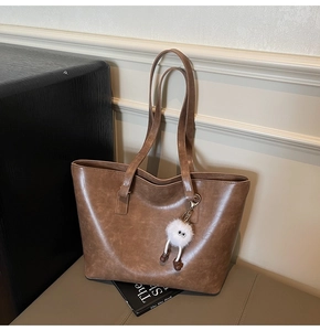 Detail of vintage brown PU leather tote bag with white plush charm in urban scene