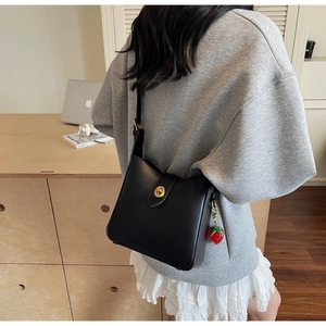 Detalle de bolso tipo cubo de cuero negro con cierre dorado y colgante de fresa