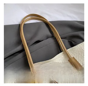 Close-up of white woven tote bag with brown leather handles and a plush bear charm