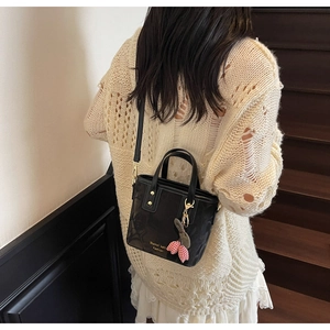 Detail of a black leather crossbody bucket bag with golden hardware and floral charm