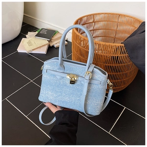 Macro detail of light blue denim bucket bag with gold padlock and dual strap buckles