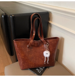 Detail of a brown tote bag with vintage texture and a cute white plush doll pendant
