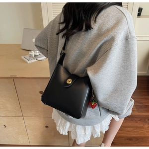 Detalle de bolso bandolera de cuero negro con hebilla dorada y colgante de fresa roja