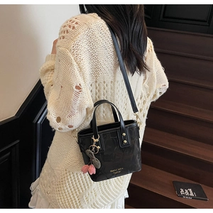 Detail view of black patent leather bucket bag with cherry charm worn as a shoulder bag