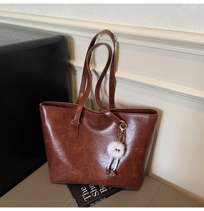 Close-up of brown textured leather tote bag with a white plush eye-shaped charm decoration