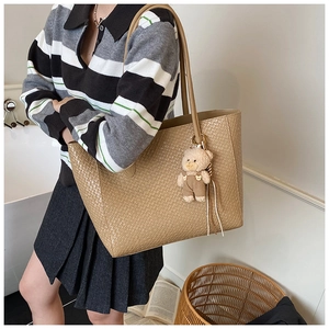 Detail of khaki tote bag with woven texture and cute teddy bear pendant on shoulder strap