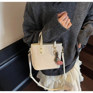 Detail of cream-white leather bucket bag with cherry charm and logo on shoulder strap