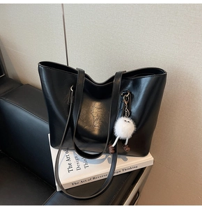 Detail of a black leather tote bag with a cute white plush charm on a black sofa