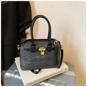 Detailed view of dark grey tweed handbag with black leather straps and gold buckle