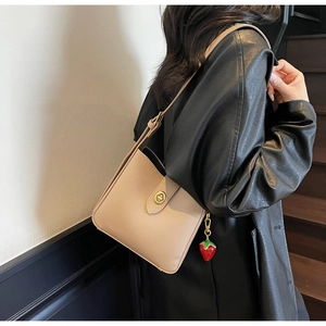 Detalle de bolso bucket beige de piel sintética con cierre dorado y colgante de fresa