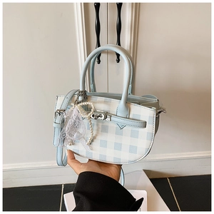 Detail of blue plaid bucket bag featuring pearl lace charm and adjustable strap