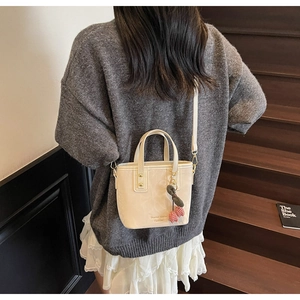 Chic beige bucket bag with cherry charm shown on model climbing wooden stairs