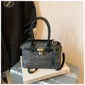 Close-up of gray tweed bucket bag featuring a gold H-lock on a silver suitcase