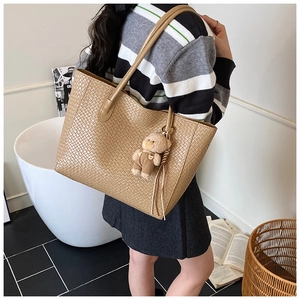 Detail view of khaki woven texture tote bag with a cute brown bear charm accessory