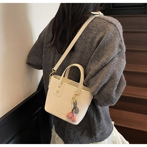 Detail of cream bucket bag with cherry charm shown on stairs by a model wearing a sweater