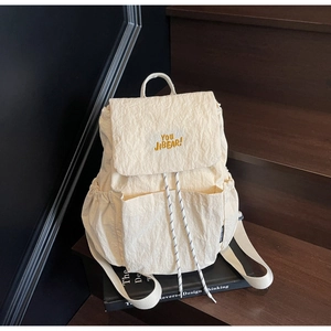 Detail view of cream nylon backpack with orange embroidery and drawstring closure