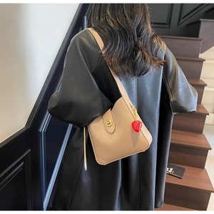 Detalle de bolso hobo beige con cierre giratorio dorado y colgante de fresa