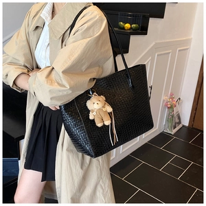 Detailed view of black woven tote bag with cute bear charm worn by a model