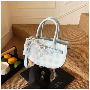 Close-up of blue and white plaid bucket bag with pearl lace bow and metal twist lock
