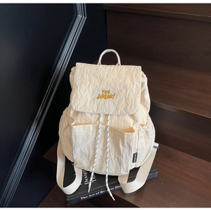 Detailed close-up of beige pleated backpack texture with yellow embroidery on stairs