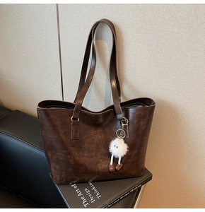 Close-up of brown PU leather tote bag texture with cute plush ball pendant detail