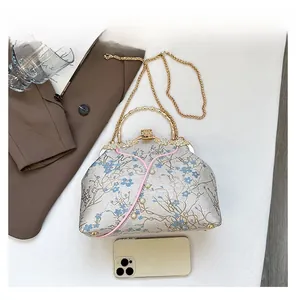 Detail view of floral cheongsam bag size compared to a smartphone with golden handle