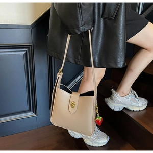 Detalle del bolso de cubo beige con cierre de giro dorado y colgante de fresa