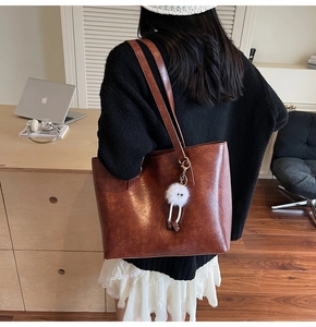 Detail of caramel brown tote bag with glossy leather texture and white plush pendant