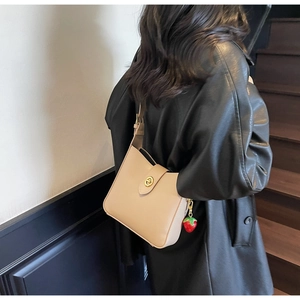 Detalle del bolso tipo cubo beige con cierre dorado y colgante de fresa decorativo