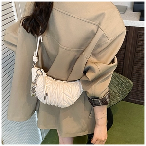 Détail d'un sac hobo matelassé beige avec plis ondulés et breloque chaîne en cœur