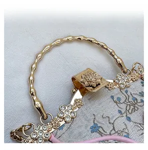 Detail view of floral embroidery on light grey silk handbag with gold metal handle