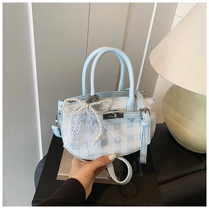 Close-up of blue plaid bucket bag with pearl lace bow and silver metal buckle