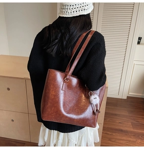 Detailed back view of a brown faux leather tote bag with a white plush doll charm