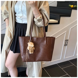 Detail of dark brown woven tote bag with a cute plush bear pendant accessory