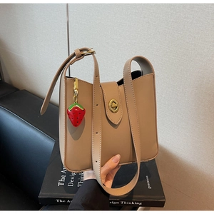 Detalle de bolso de cuero caqui con cierre dorado y colgante de fresa decorativo