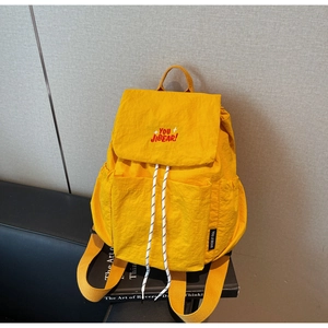 Detail of yellow nylon backpack featuring drawstring closure and red embroidery text
