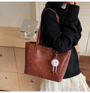Brown vintage leather tote bag with fluffy charm shown in a professional work setting
