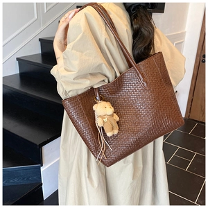 Detail shot of a large brown woven tote bag featuring a cute teddy bear plush charm accessory