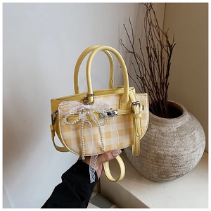 Detail of yellow checkered bucket bag with lace bow, pearl charm and metal lock closure