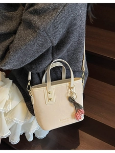 Chic cream bucket bag with top handles and a cherry charm shown on a model