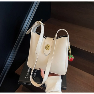 Detalle del bolso bandolera crema con cierre dorado y accesorio de colgante fresa